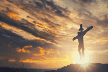 a silhouette of jesus carrying a cross with the sun shining through the clouds