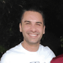 a man wearing a white t-shirt with a logo on it smiles for the camera