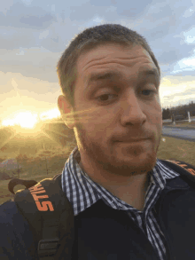 a man wearing a stihl backpack stands in front of a sunset