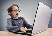 a young boy wearing glasses is looking at a laptop computer .