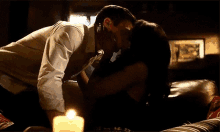 a man and a woman are kissing on a couch next to a lit candle .