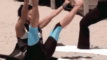 a woman is doing a yoga pose on a beach while a man stands behind her .