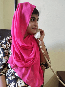 a woman wearing a pink scarf talks on a phone