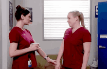 two nurses in red scrubs are shaking hands in front of a blue door that says first aid