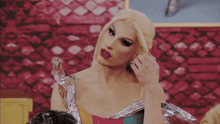 a drag queen is putting on her earrings in front of a red brick wall