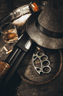 a hat a knuckle duster a shotgun and a glass of whiskey are on a wooden table