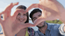 a man and woman are making a heart with their hands