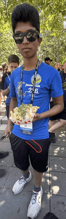 a young man wearing sunglasses and a blue shirt with the number 28 on it is holding a plate of food