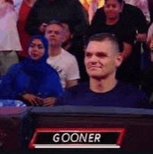 a man is sitting in a crowd with a name tag that says gooner on it .