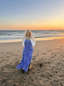 a woman in a blue and white dress stands on a beach