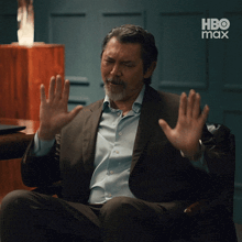 a man in a suit and blue shirt is sitting in a chair with his hands up in front of a hbo max logo