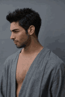 a shirtless man wearing a gray robe is standing in front of a gray wall .