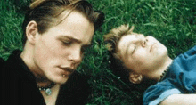 two young men are laying in the grass and one of them is sleeping .