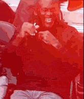 a man in a red shirt is sitting in a chair laughing .