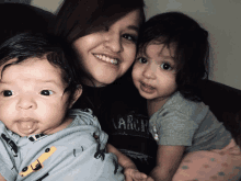 a woman is holding two children one of whom is wearing a shirt that says arch