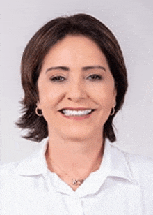 a woman wearing a white shirt and necklace is smiling for the camera .