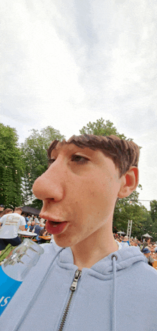 a man wearing a blue hoodie has a large nose and a bottle of water in his hand