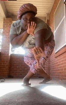 a woman is standing on a porch in front of a brick building with her hands on her face .