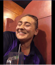 a woman in a purple shirt is smiling while holding a glass with a straw in it