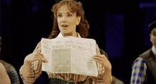 a woman is holding a newspaper that says ' newsies stop the world news ' on it .