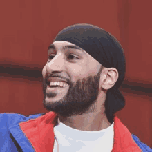 a man with a beard wearing a headband and a blue jacket is smiling .