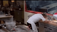 a man in a white chef 's uniform is kneeling down in a kitchen