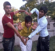 three young men are making a heart shape with their hands in a park .