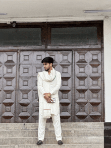 a man in a white outfit stands on stairs in front of a wooden door