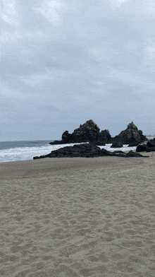 a beach with rocks in the distance and a cloudy sky