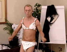a man in a bra and underwear stands in front of a dry erase board
