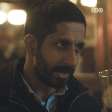 a man with a beard is smiling and holding a glass with a slice of lemon on it in front of a hbo logo