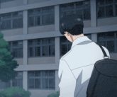 a man with a black backpack stands in front of a building with many windows
