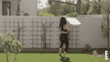 a woman is carrying a large piece of pizza in her hand while standing in front of a fence .