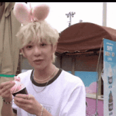 a man wearing bunny ears is eating ice cream from a cup