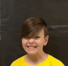 a young boy wearing a yellow t-shirt is smiling for the camera .