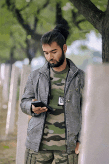 a man wearing a camouflage shirt and a gray jacket looking at his phone