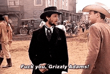 two men in suits and hats are standing next to each other on a dirt road and talking .