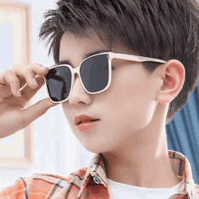 a young boy wearing a plaid shirt and sunglasses looks at the camera