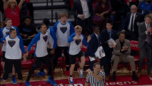 a man in a suit holds a clipboard while a group of basketball players wearing shirts that say be brave