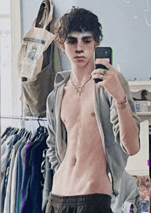 a shirtless young man taking a selfie in front of a mirror with a bag hanging on the wall