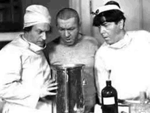 three men are standing next to each other in a room looking at a bottle .