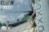 a man climbs a ladder in front of a green helicopter and a sign that says cloak bagger