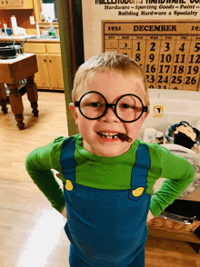 a little boy wearing glasses and overalls is standing in front of a calendar that says december 1931