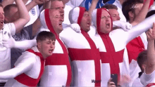 a group of men wearing white and red outfits with a cross on them are standing in a crowd .