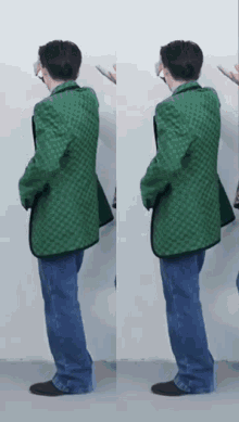 a man in a green jacket and blue jeans is standing in front of a wall