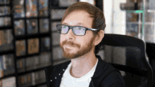 a man with a beard and glasses is sitting in a chair in front of a shelf of video games .