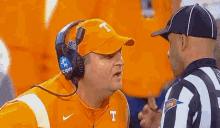 a man wearing a hat with the letter t on it is talking to a referee on a football field .