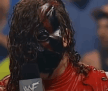 a wrestler with blood on his face is talking into a microphone while wearing a mask .