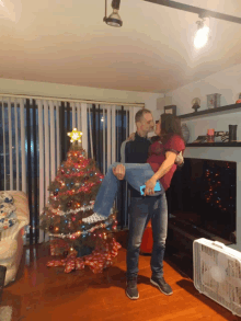 a man holds a woman in his arms in front of a christmas tree