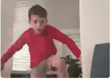 a young boy in a red shirt is jumping on a couch in a living room .